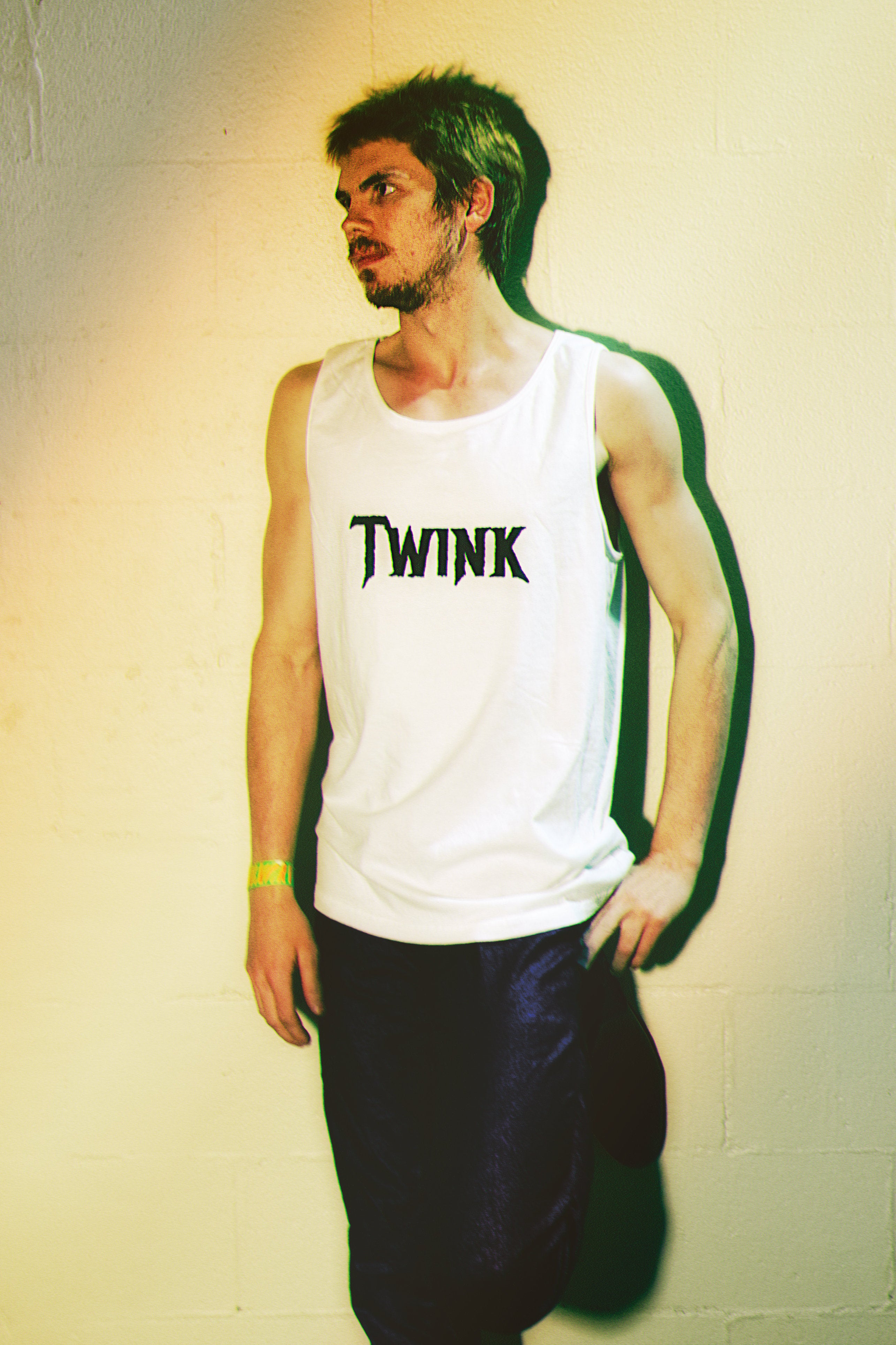 Person wearing a white tank top with 'TWINK' text against a plain background